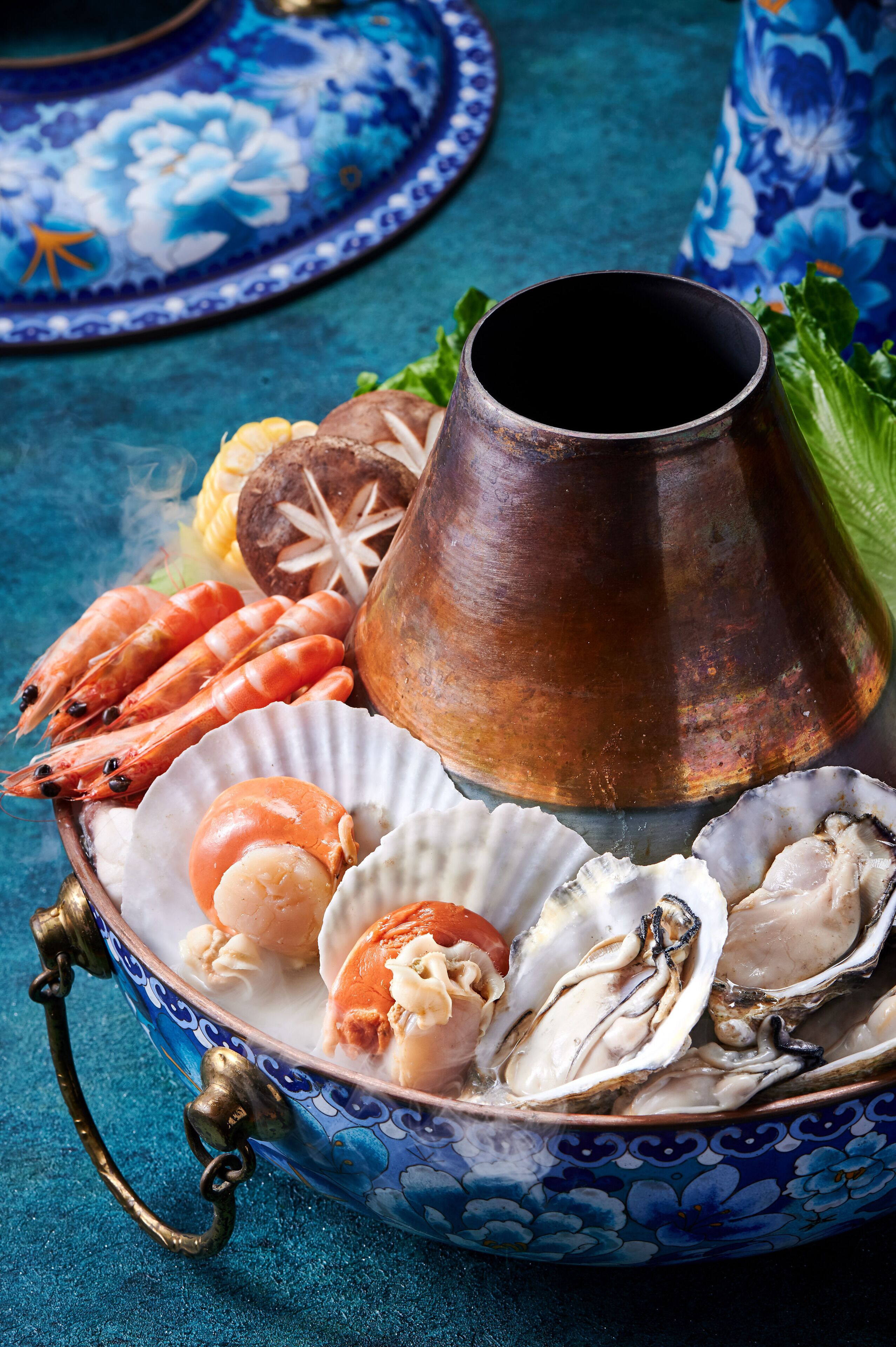A decorative bowl with seafood, a copper pot, and a blue patterned plate.