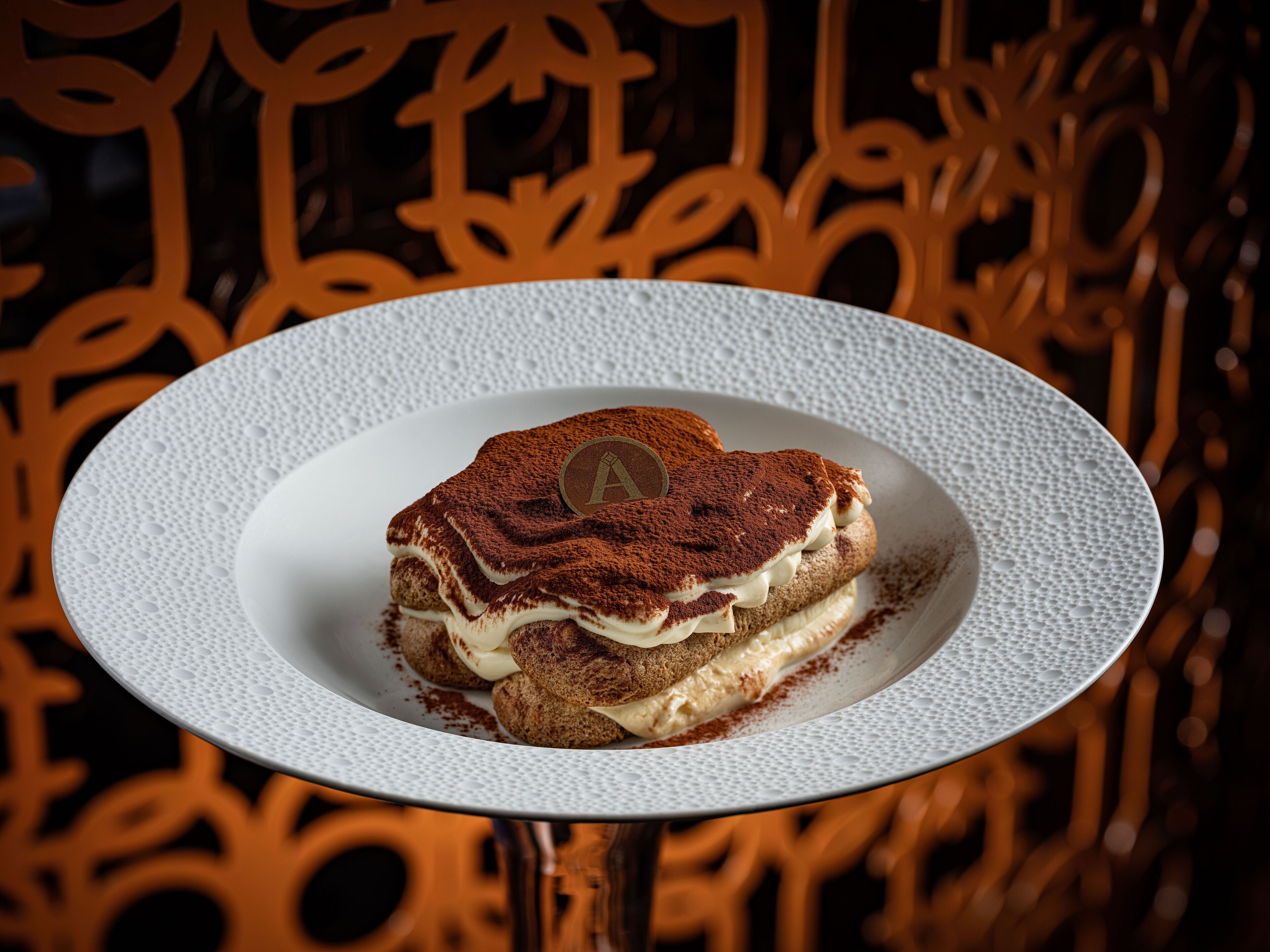 Un postre sobre un plato blanco con superficie texturizada, colocado sobre una mesa con superficie reflectante.