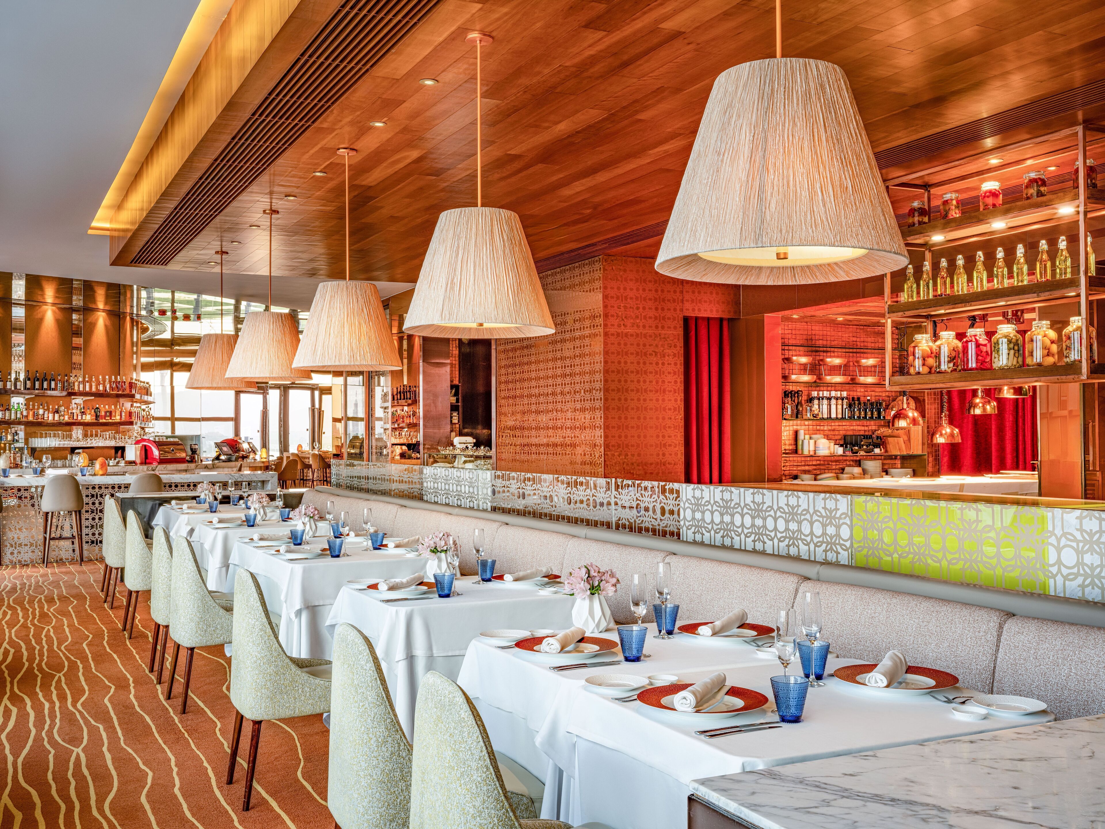 A restaurant with multiple tables set for dining, a bar area with shelves of bottles, and a patterned carpet.