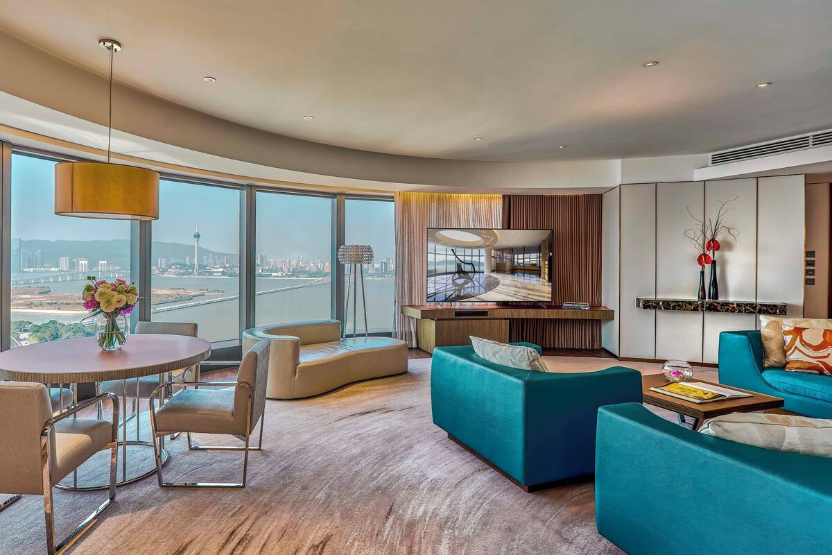 Une chambre d’hôtel moderne dotée d’une grande télévision, de sièges confortables, d’un coin repas et offrant une vue sur le paysage urbain.
