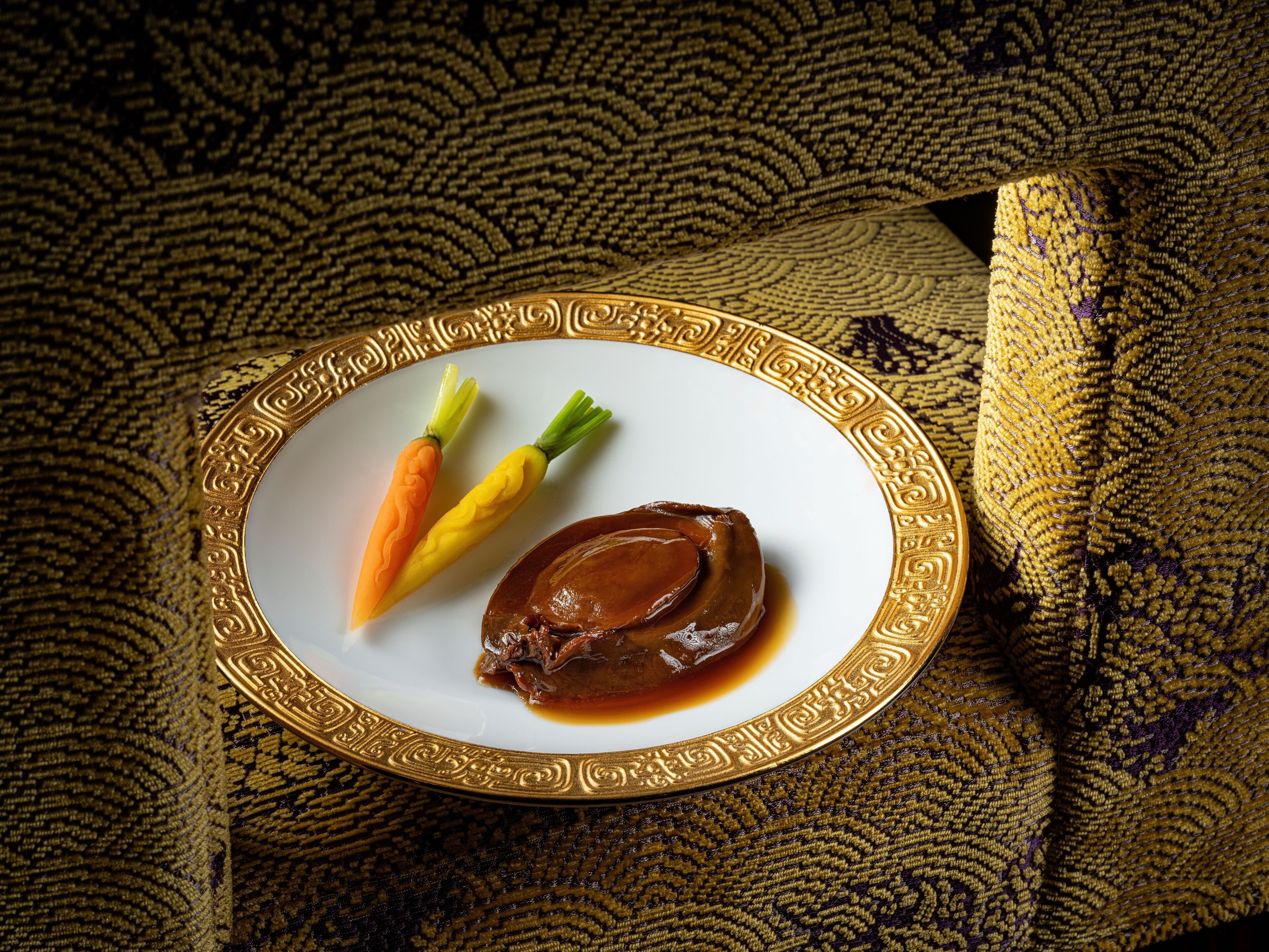 A plate with a piece of meat and two vegetables on a patterned fabric background.