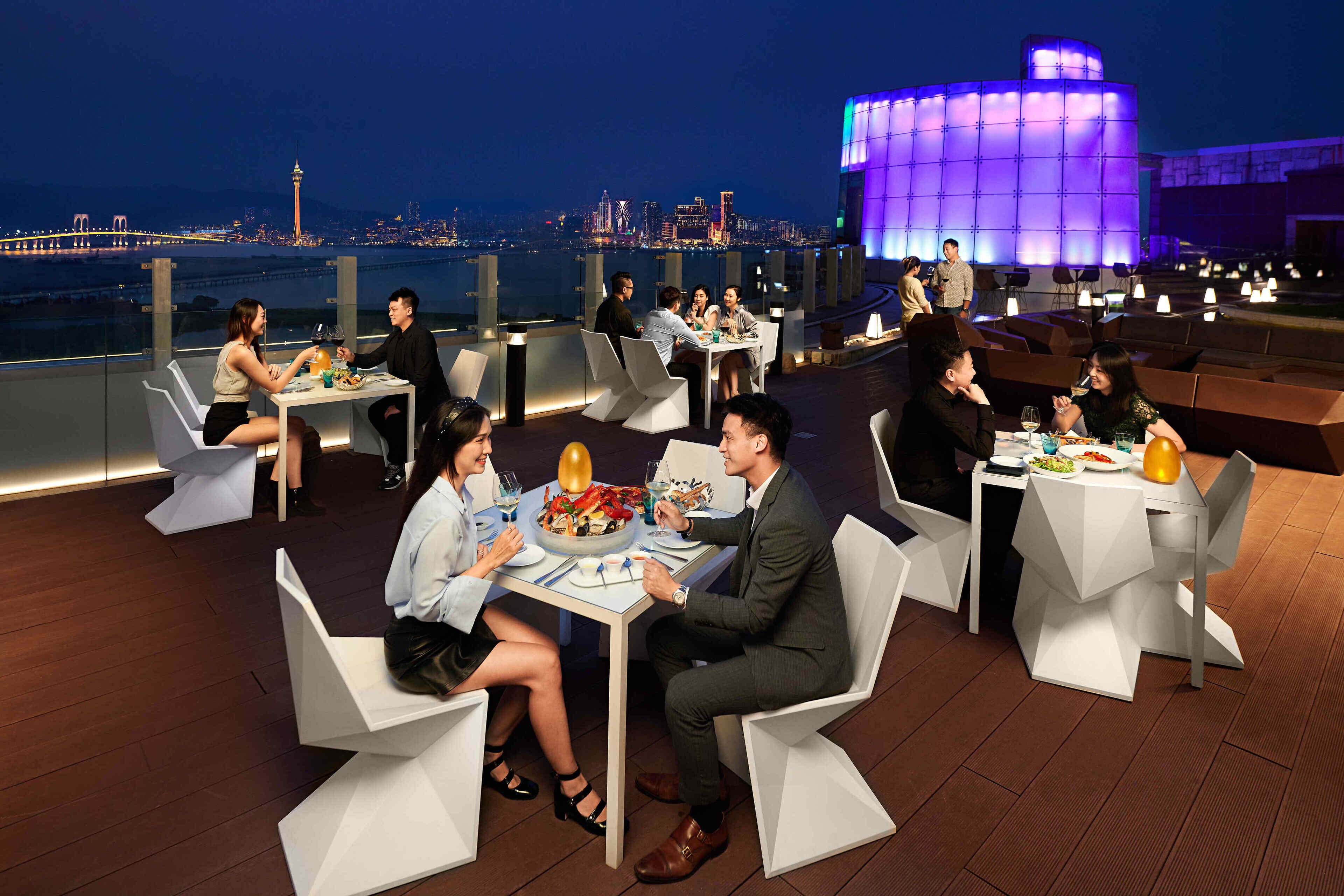Un espace extérieur aménagé pour les repas, avec des meubles blancs au design moderne et une vue sur le paysage urbain en arrière-plan.
