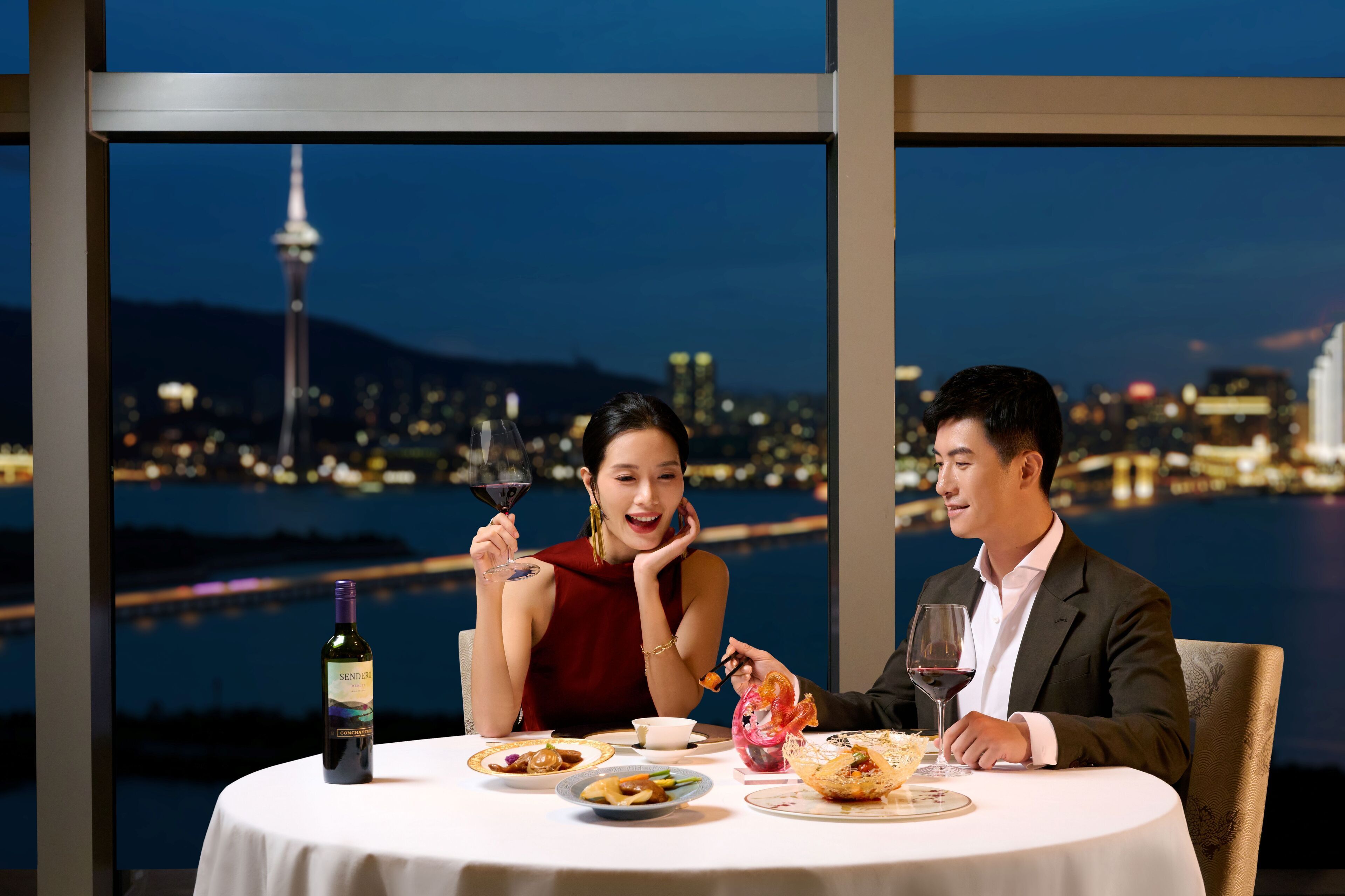 Una pareja cenando en una mesa con vista a un paisaje urbano, que incluye una torre, en un ambiente moderno.
