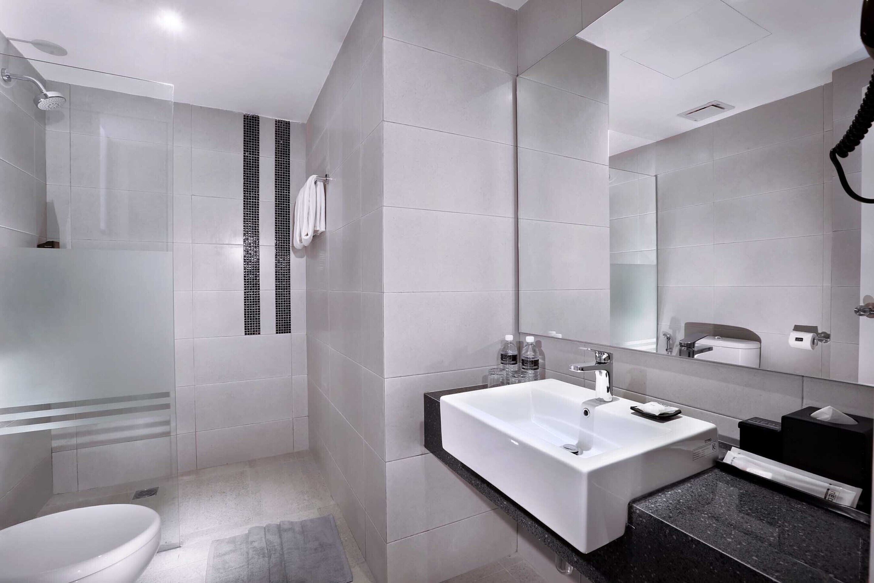 A modern bathroom with a glass-enclosed shower, a white sink with a black countertop, and a large mirror above the sink.