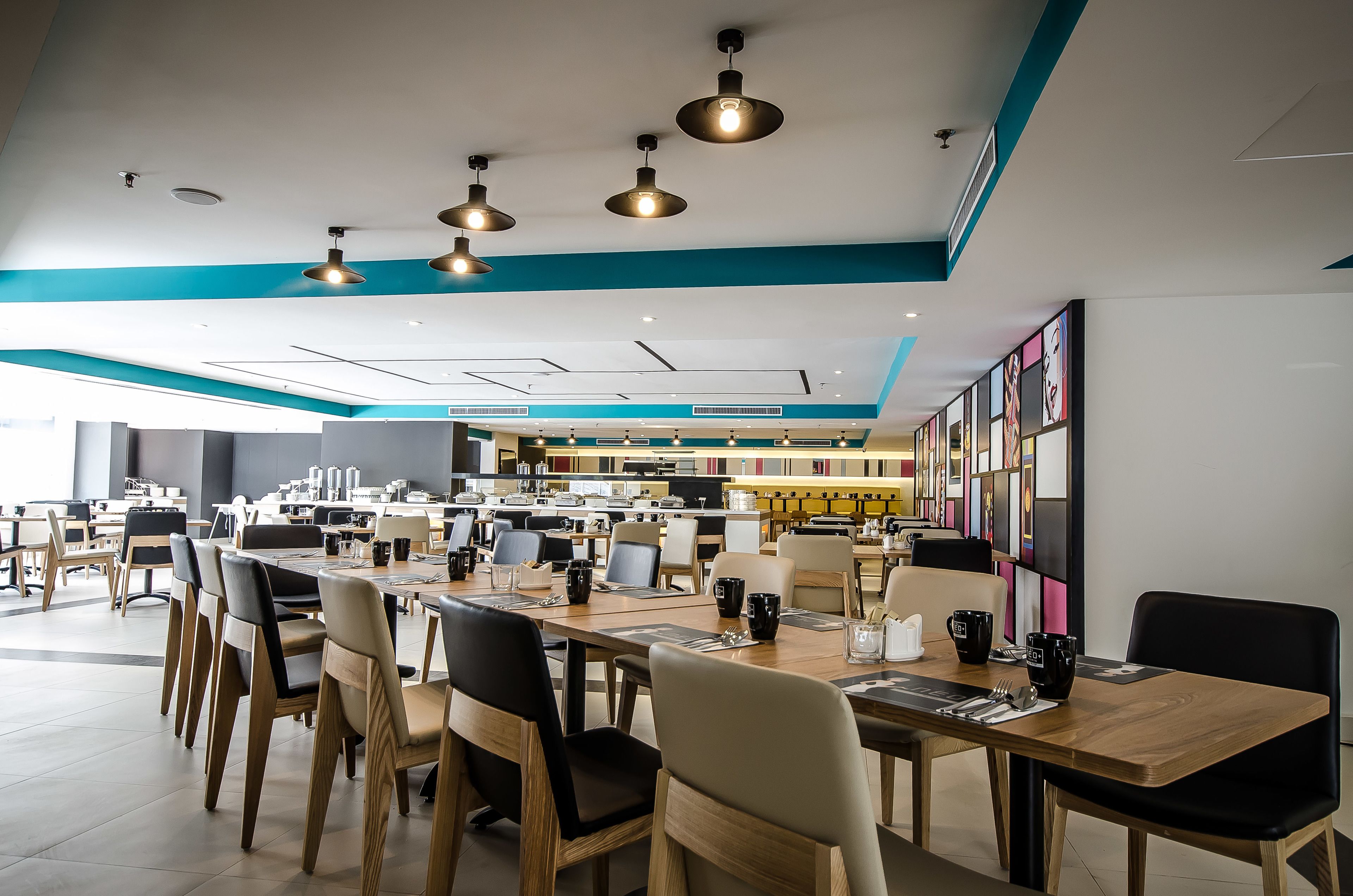 Un comedor moderno con varias mesas y sillas, luces de techo y una zona de cocina al fondo.