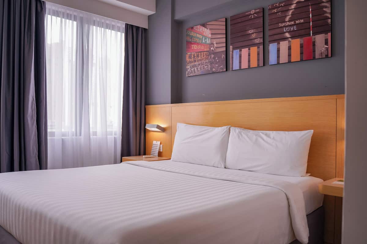A neatly made bed with white linens, a wooden headboard, and a nightstand with a lamp.