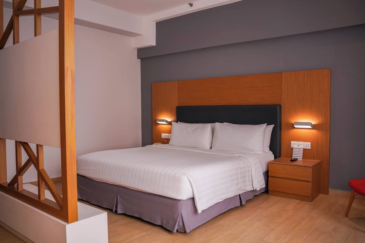 A modern bedroom with a large bed, wooden headboard, bedside lamps, and a red chair.