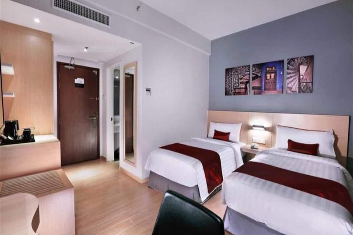 A hotel room with two beds, a desk, and a chair. There is a door leading to another room.