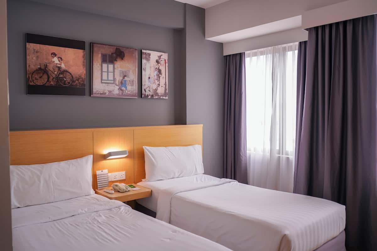 A hotel room with two beds, a wooden headboard, a bedside table with a phone, and artwork on the wall.