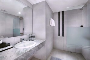 Un baño moderno con lavamanos de mármol, un espejo grande y una ducha con cerramiento de vidrio.