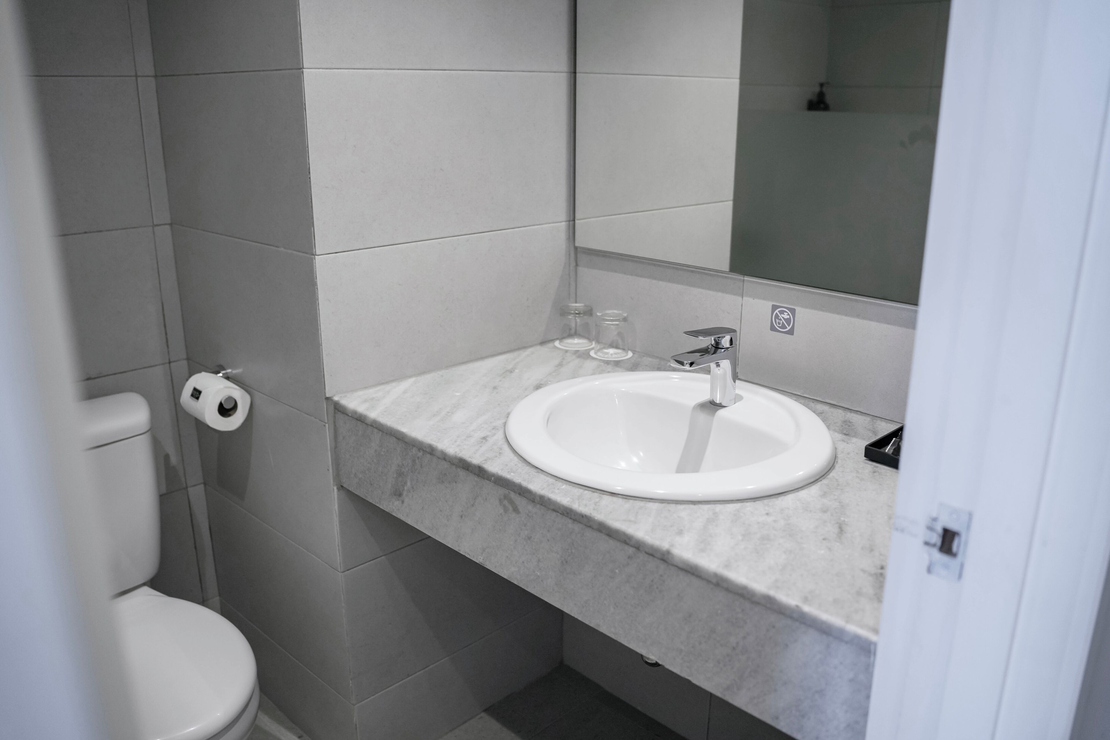 A bathroom with a white toilet, a sink with a mirror above it, and a toilet paper roll on the wall.