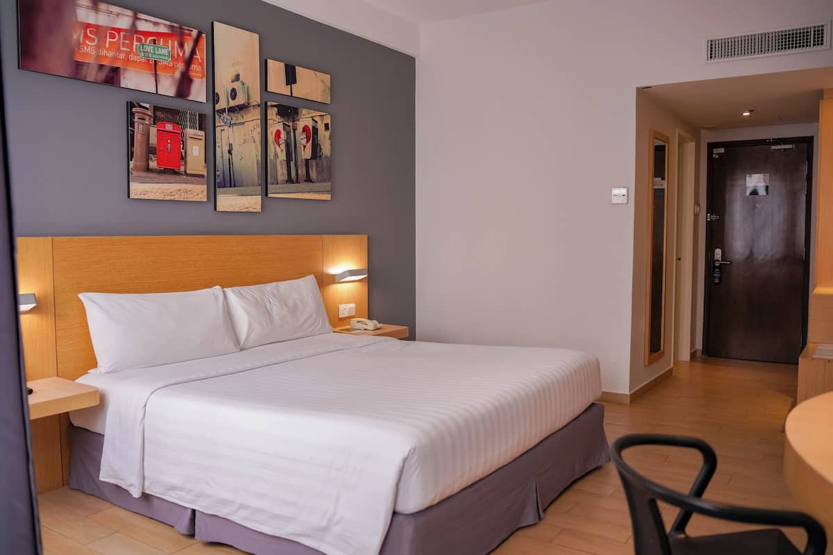 A hotel room with a large bed, bedside tables, a desk, and a chair. There are wall art pieces above the bed and a door to the right.