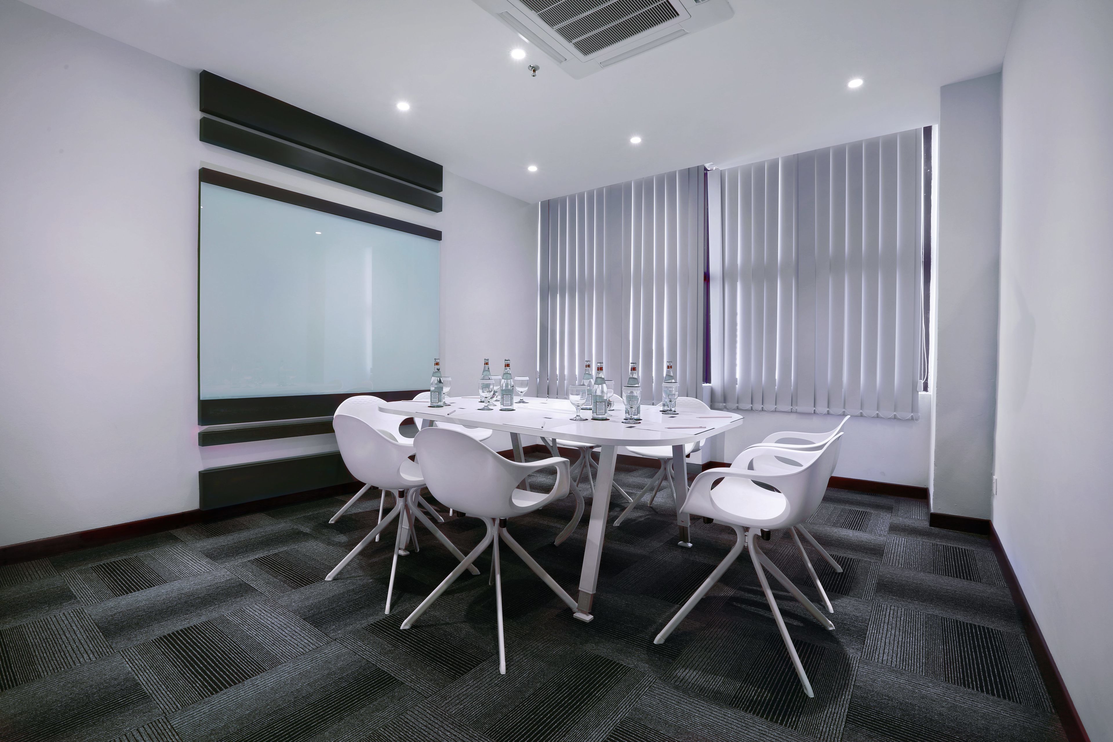 A conference room with a round table, white chairs, and a glass partition.