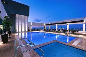 Una piscina en la azotea con vistas despejadas al horizonte de la ciudad, rodeada de sillones de descanso y plantas en macetas.