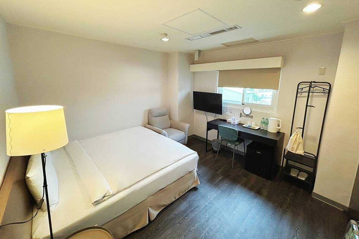A hotel room with a bed, desk, chair, TV, and a clothes drying rack.