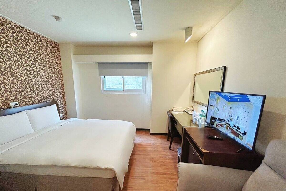 A hotel room with a large bed, a desk with a computer, a TV, and a window.