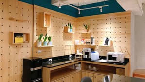 A compact kitchen with wooden walls, a black countertop, and various appliances including a coffee machine and microwave. - Trust Hotel (Tainan)
