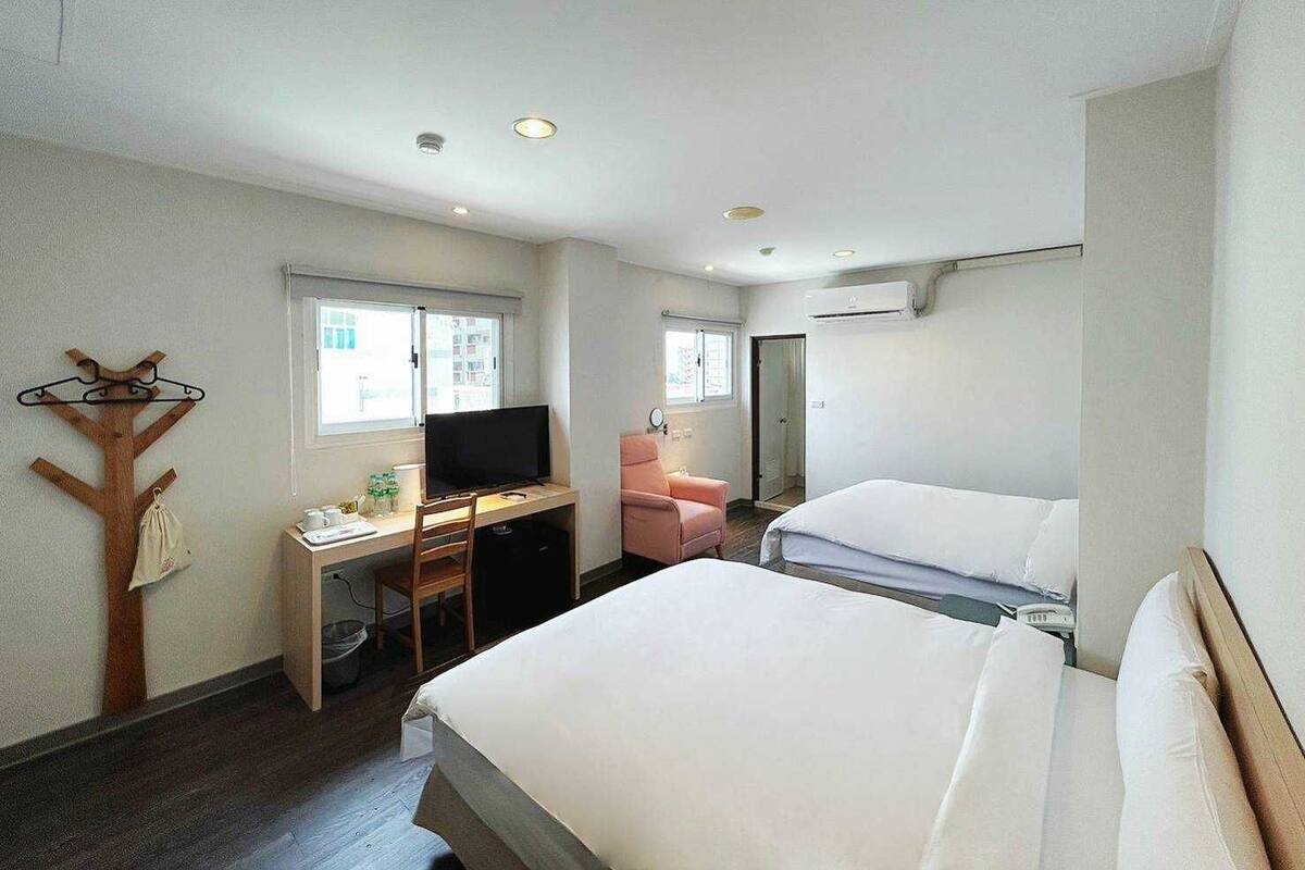A hotel room with two beds, a desk with a television, a chair, and a coat rack.