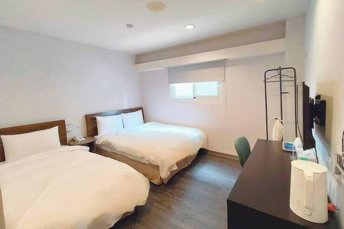 A hotel room with two beds, a desk, a chair, a TV, and a window.