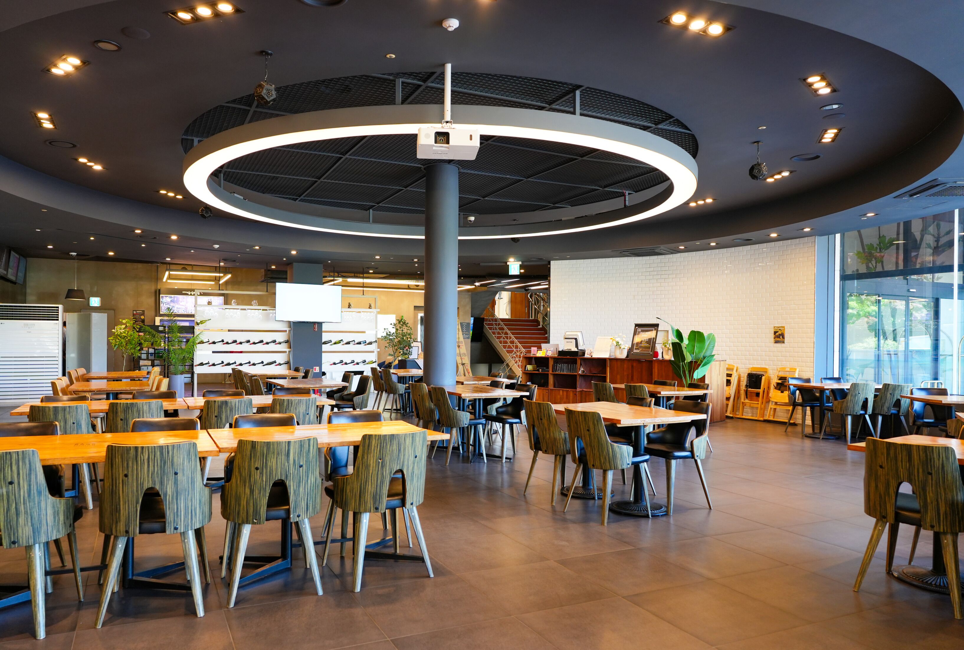 A spacious indoor area with multiple tables and chairs, a central column, and a staircase leading to an upper level.
