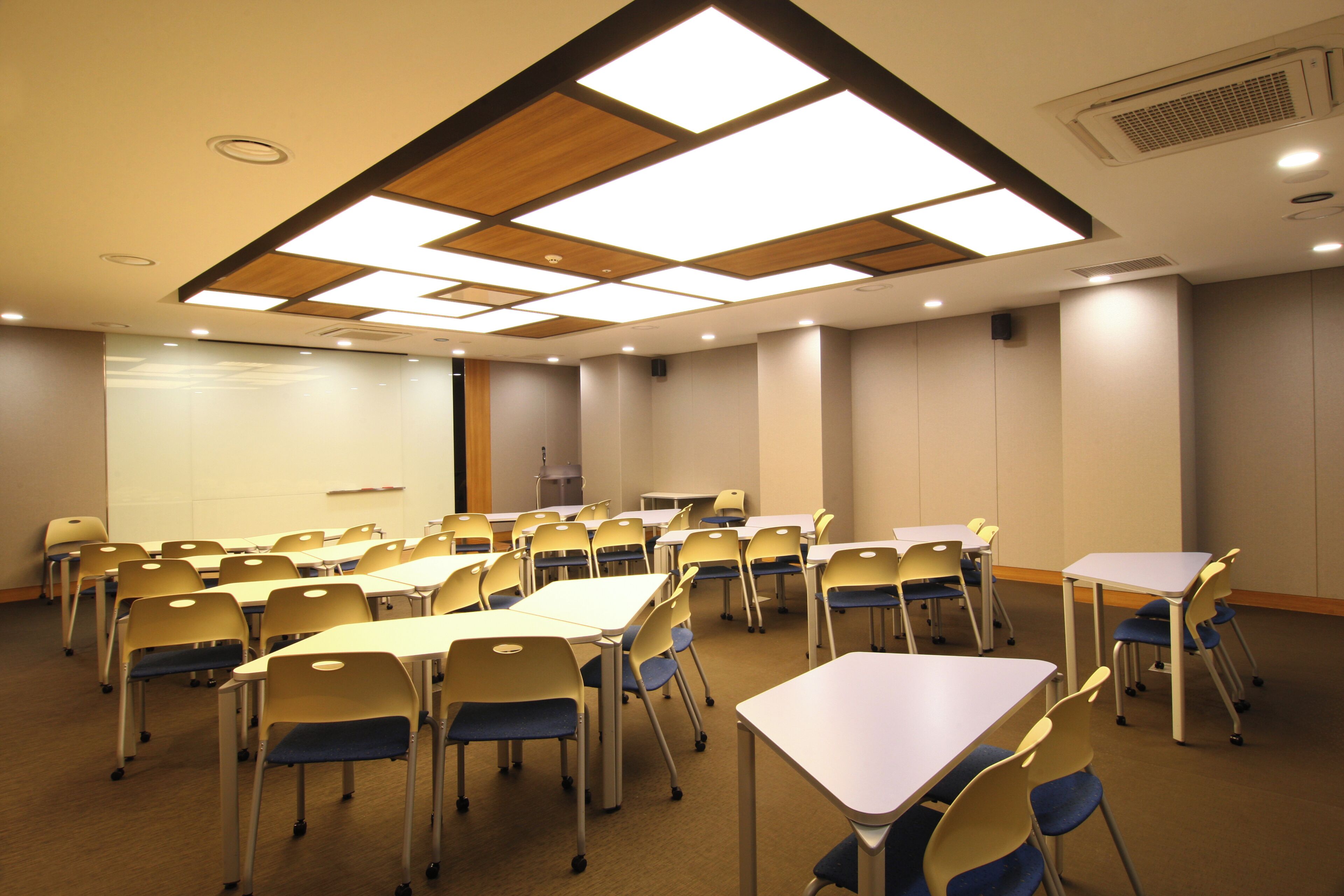 Un salón de conferencias con mesas y sillas, una pantalla de proyector y un diseño de techo de madera.