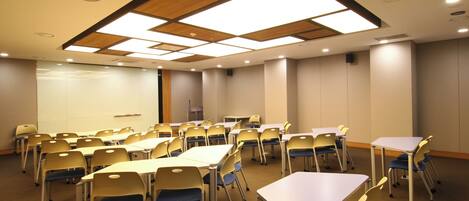 Un salón de conferencias con mesas y sillas, una pantalla de proyector y un diseño de techo de madera.