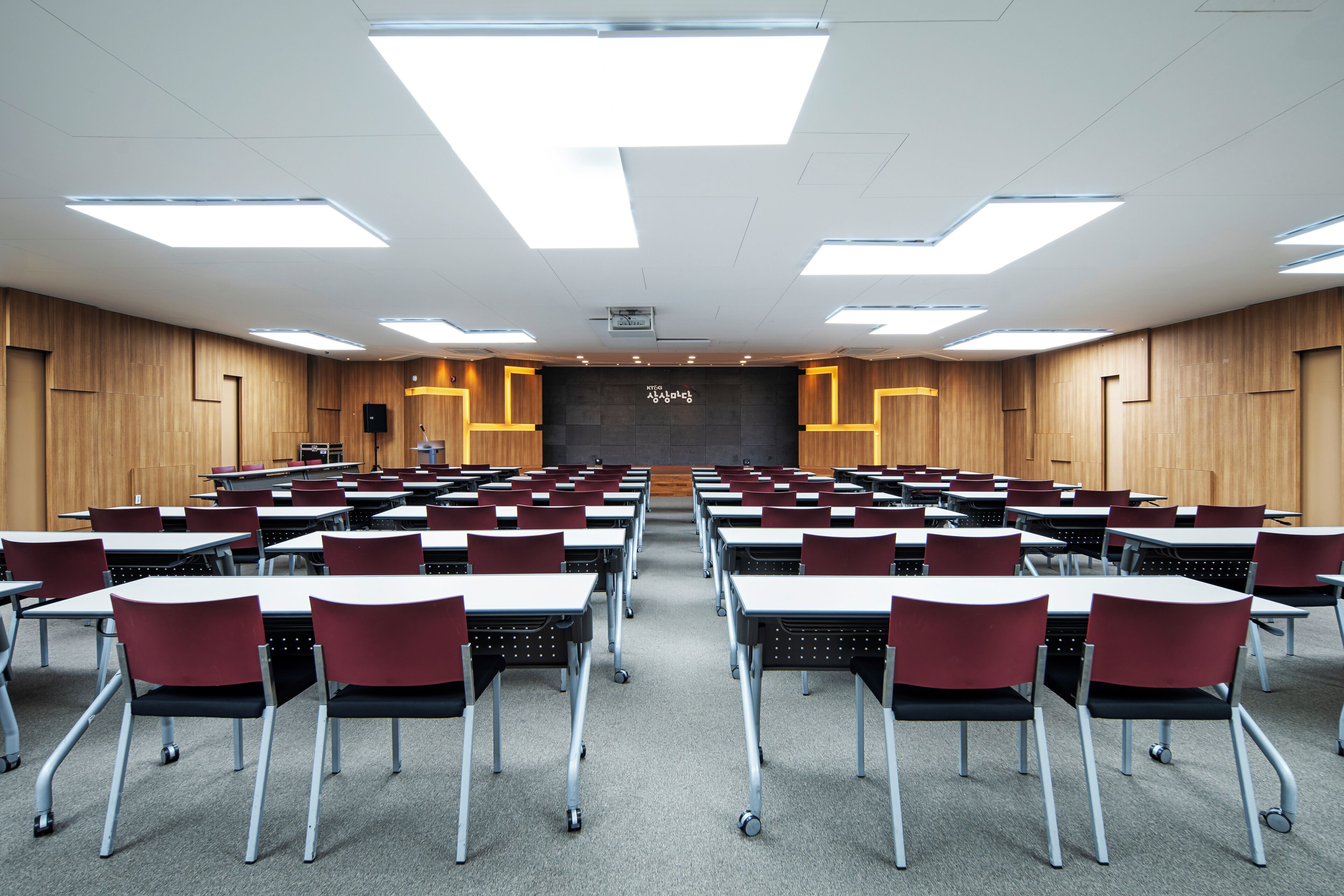 A conference room with tables and chairs, a podium, and a projector screen.