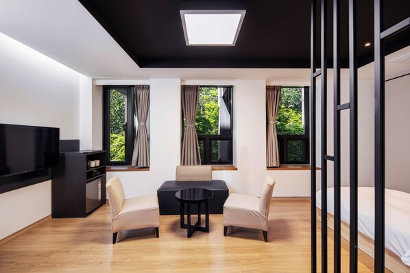 A modern room with a sofa, two chairs, a small table, a TV, and three windows with curtains. - Sangsangmadang Chuncheon Stay Hotel (Chuncheon)