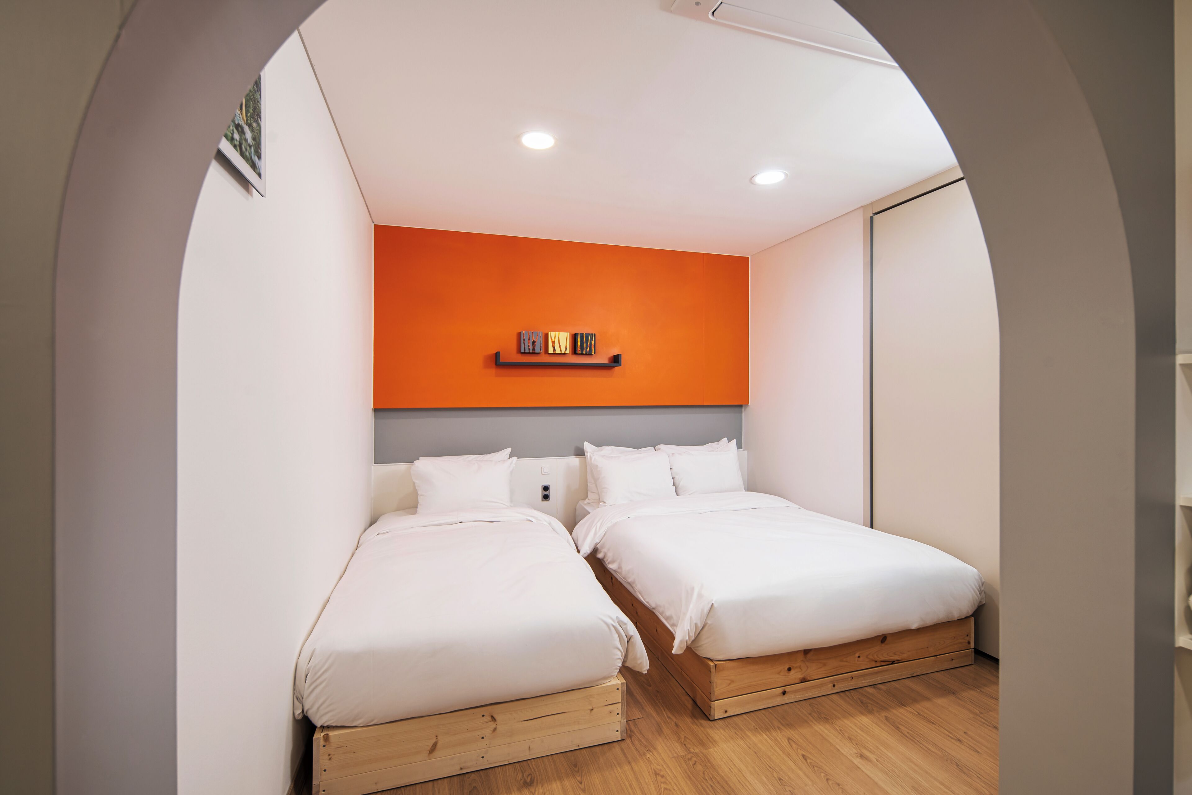 Un dormitorio con dos camas, una pared de acento naranja y suelo de madera.