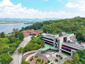 A modern building with a green roof, surrounded by lush greenery and a body of water.