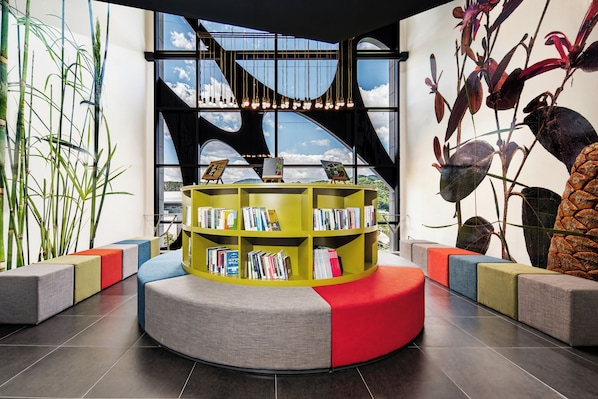 Une bibliothèque moderne dotée d’une bibliothèque centrale, d’espaces de lecture et de grandes fenêtres offrant une vue sur le ciel.