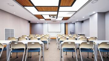 Une salle de conférence équipée de tables et de chaises, d’un écran de projection et d’un décor de plafond en bois.