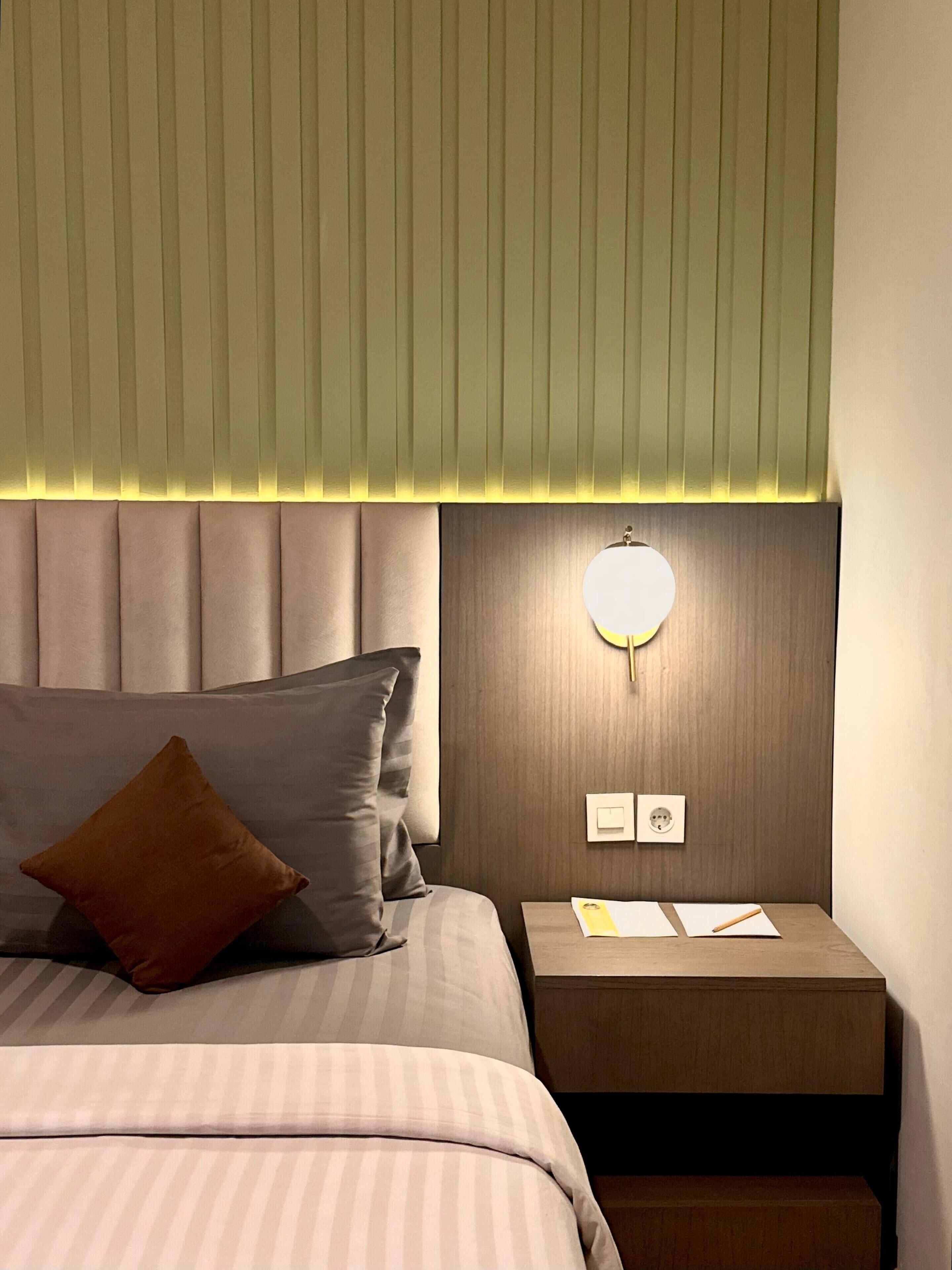 A neatly arranged hotel room with a bed, a nightstand, and a wall-mounted light fixture.