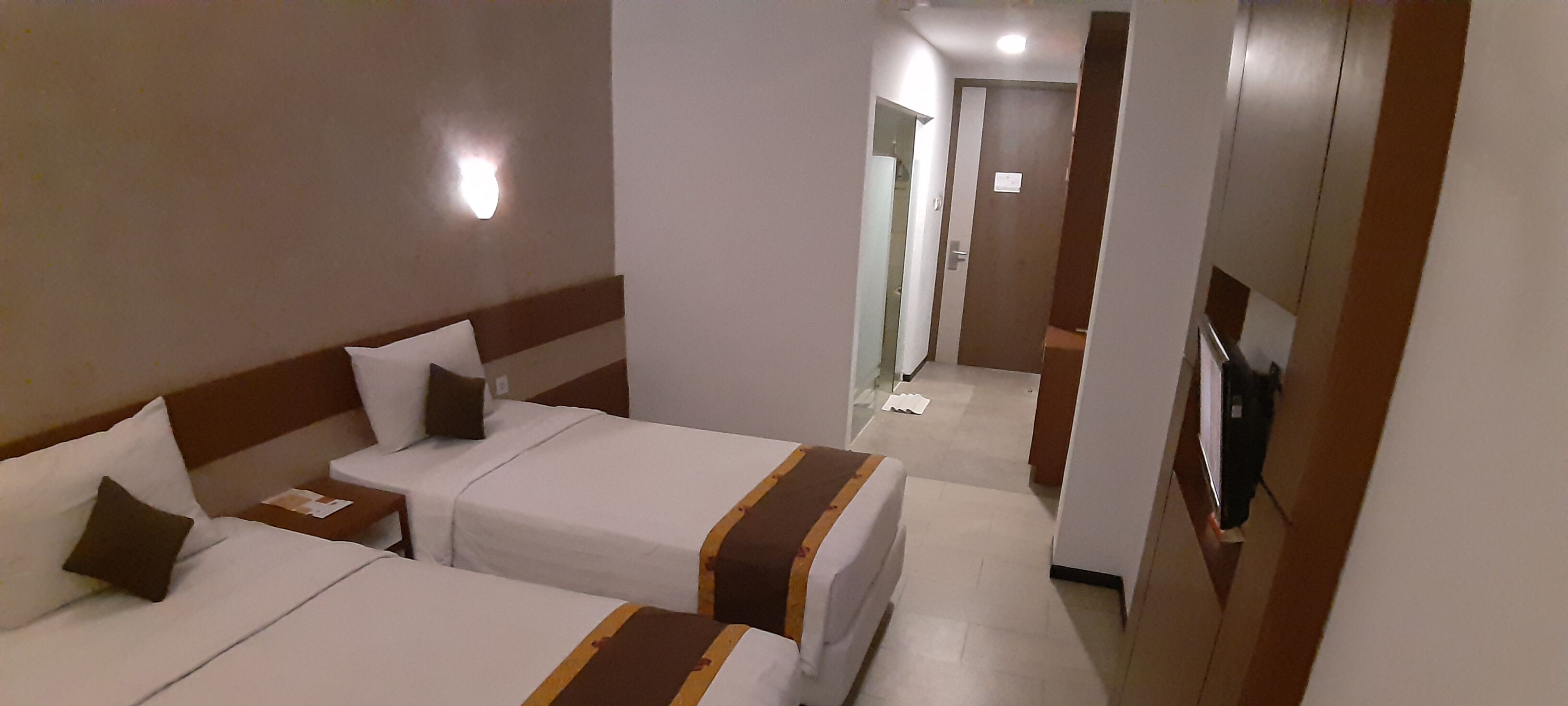 Een hotelkamer met twee bedden, een televisie en een gang naar een badkamer.
