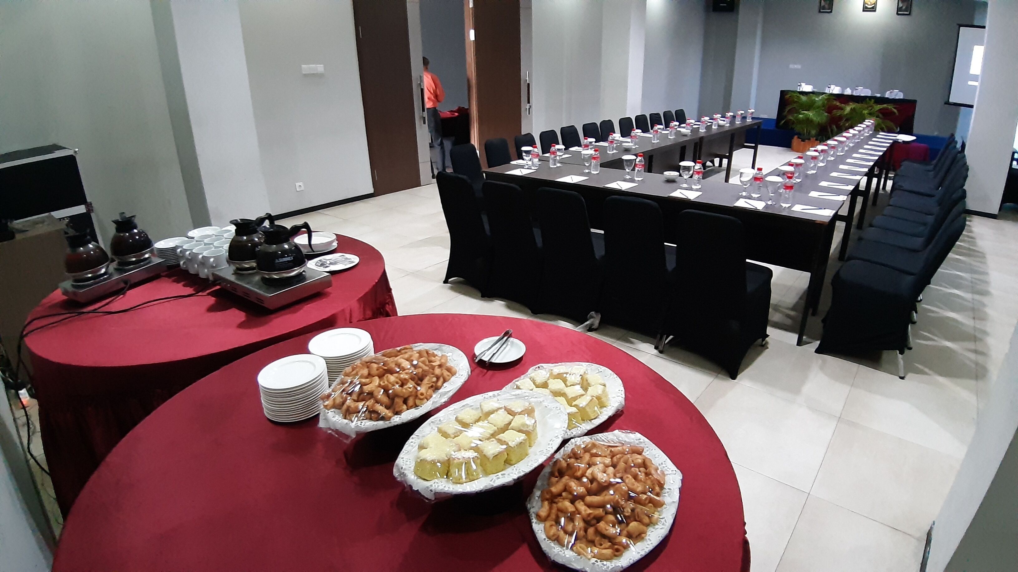Un salón de conferencias con una larga mesa dispuesta para una reunión, una mesa de buffet con diferentes opciones de comida y una estación de café.