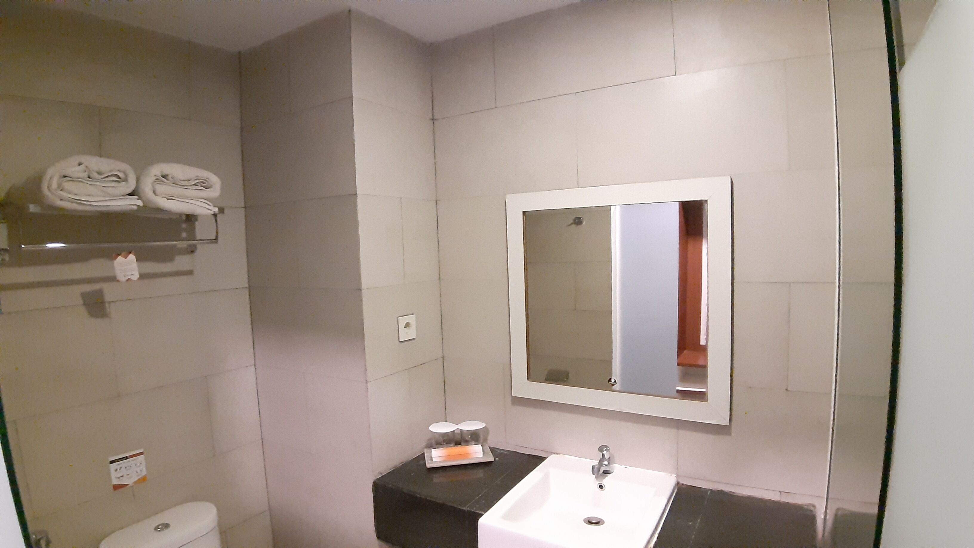Un baño con lavamanos blanco, un espejo y un toallero con toallas dobladas.