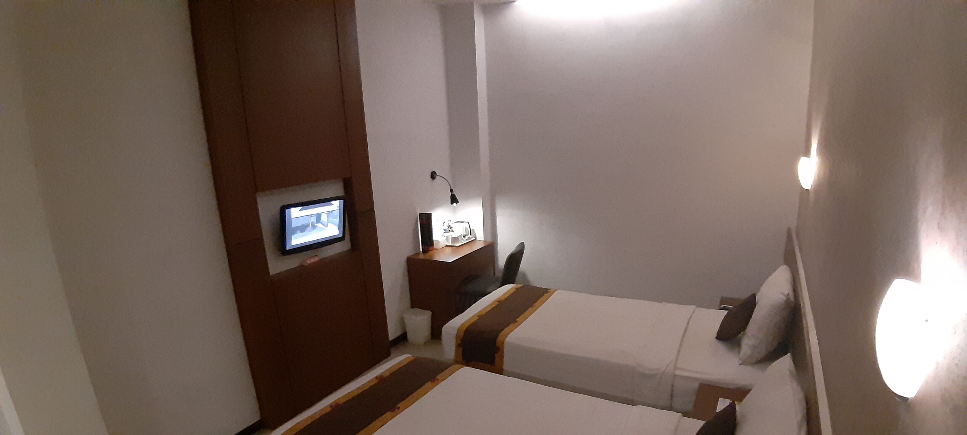 Une chambre d’hôtel avec deux lits, une télévision, un bureau avec une lampe et une petite fenêtre.