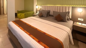 Une chambre d’hôtel avec un grand lit, un canapé vert, une table de chevet avec une lampe et une tête de lit agrémentée de stores verticaux.