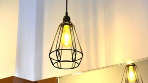 Une salle de bain moderne dotée d’une douche à parois de verre, d’un mur d’accent en bois et de deux suspensions lumineuses aux ampoules apparentes.