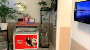 A room with a large TV on the wall, a vending machine with a GB Glace logo, a potted plant, and a glass display case with various items. - Hällefors Vandrarhem & Kanotcenter - Hostel (Hallefors)
