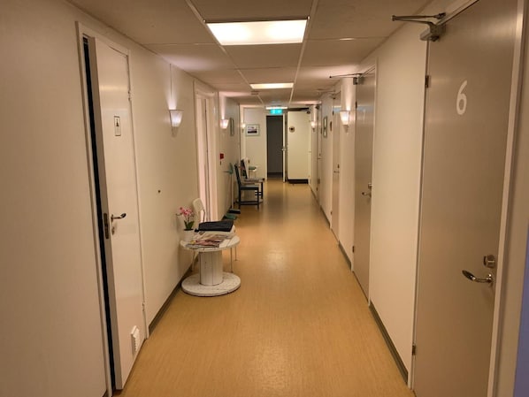 A hospital corridor with doors numbered, a small table with magazines, and a chair. - Hällefors Vandrarhem & Kanotcenter - Hostel (Hallefors)