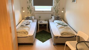 A small, well-lit room with two single beds, a small table, a chair, and a window with curtains. - Hällefors Vandrarhem & Kanotcenter - Hostel (Hallefors)