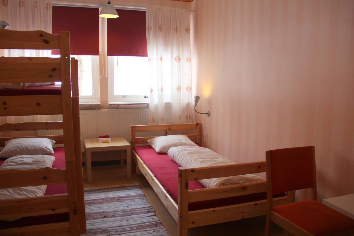 A dormitory room with bunk beds, a single bed, a small table, and a chair.