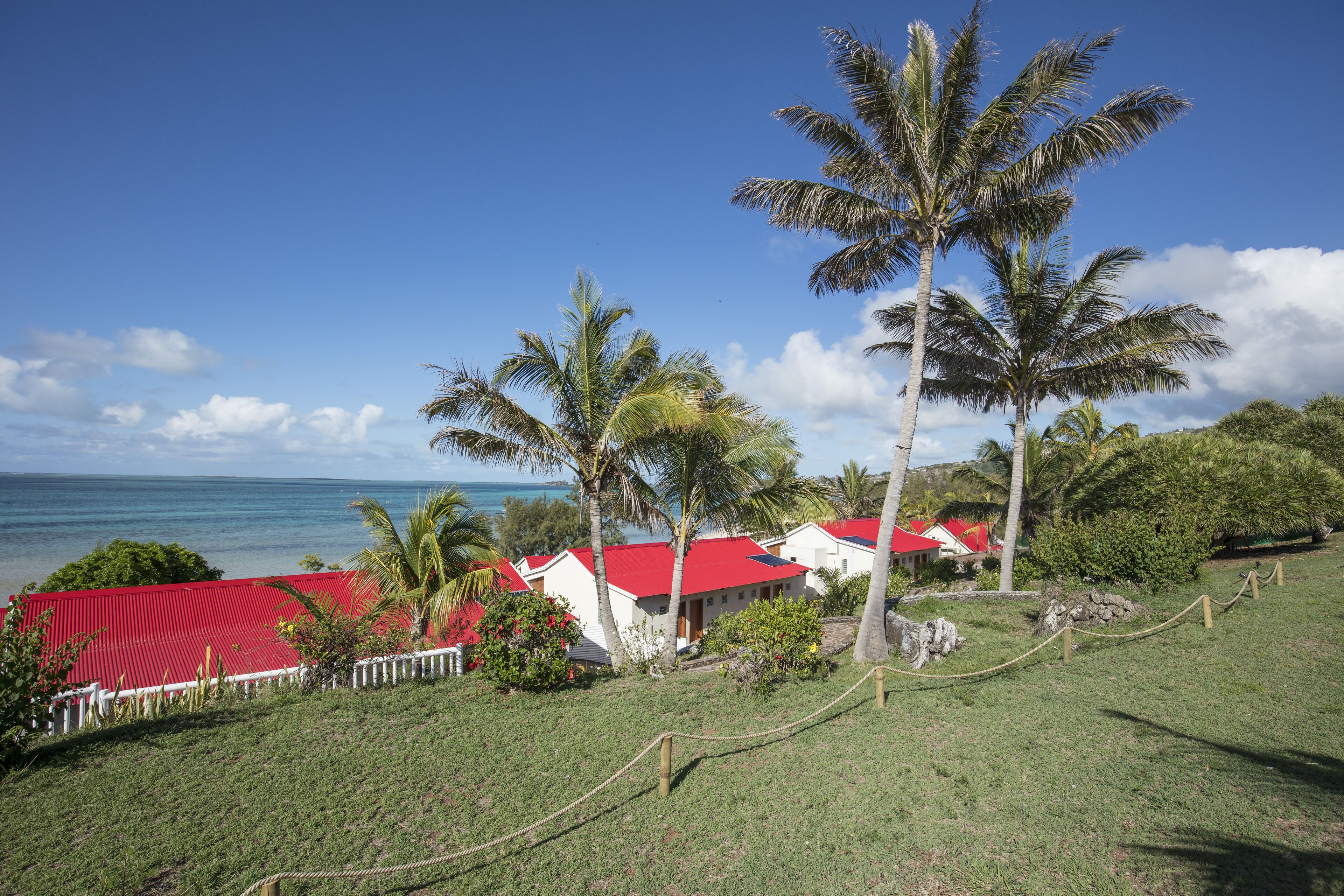 A coastal property with red-roofed buildings, palm trees, and a view of the ocean.