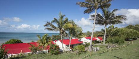 A coastal property with red-roofed buildings, palm trees, and a view of the ocean.