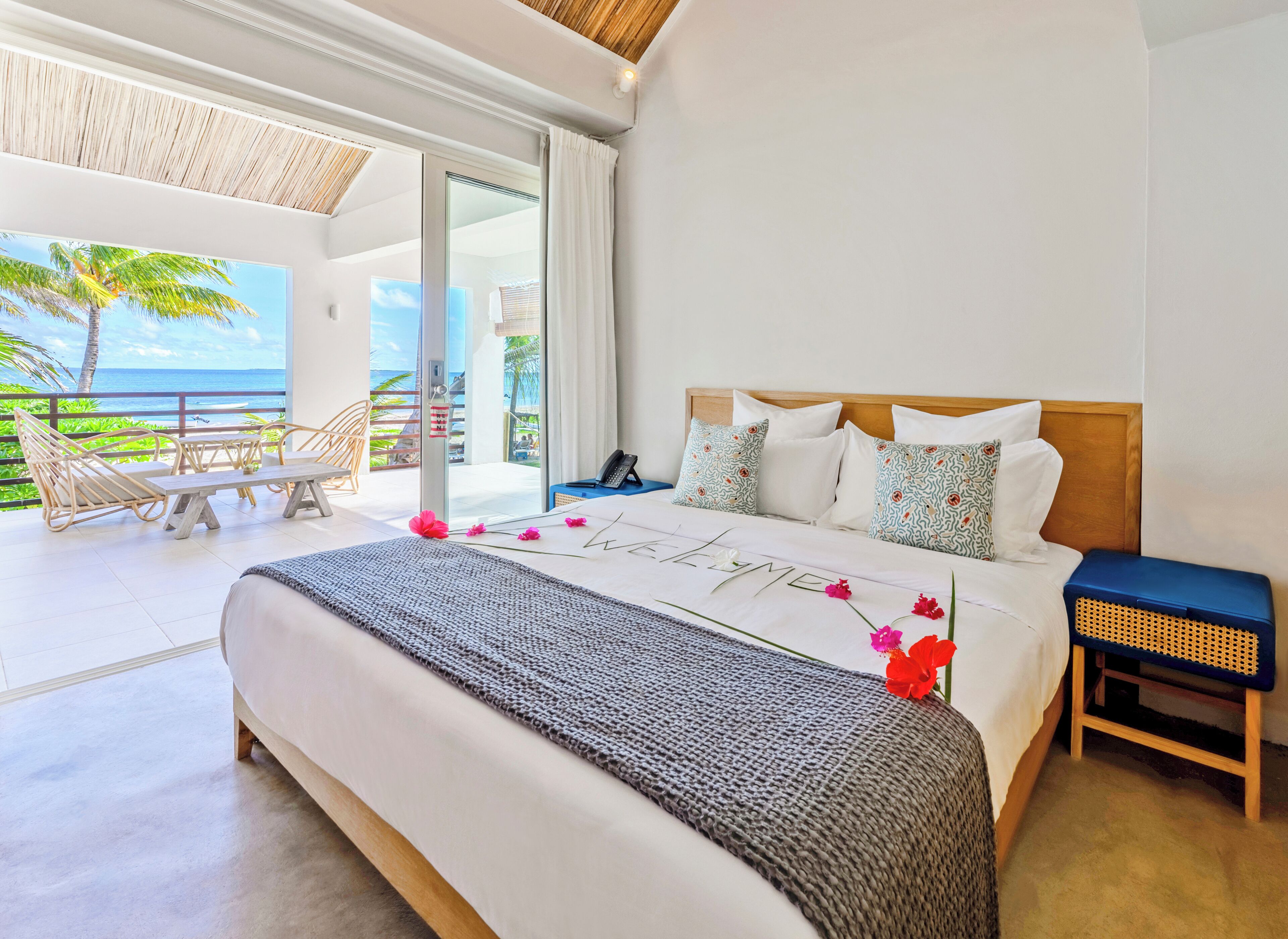 A bedroom with a large bed, a wooden headboard, and a view of the ocean through a sliding glass door.