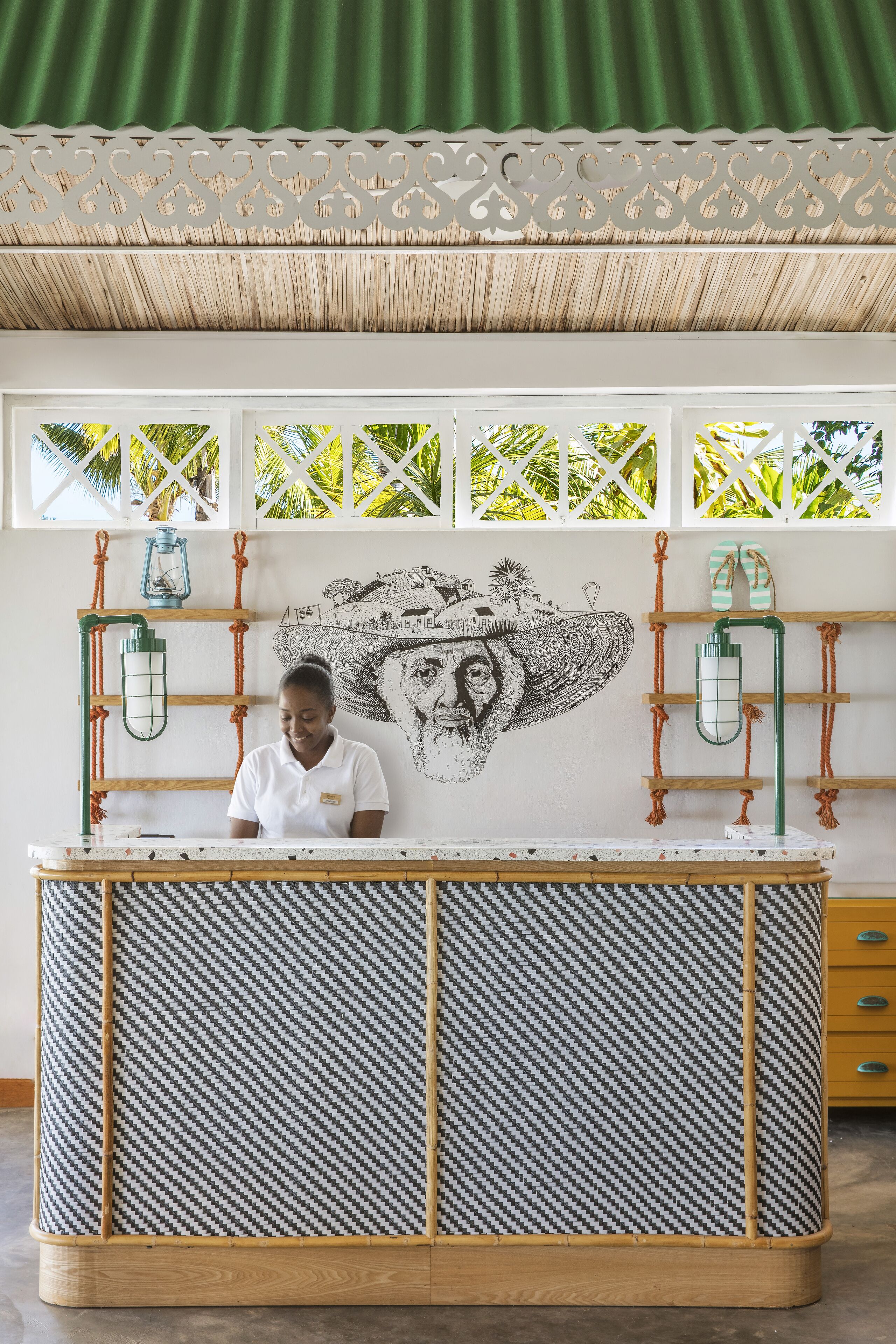 A reception desk with a patterned design, a mural, and a view of palm trees through the windows.