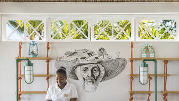 A reception desk with a patterned design, a mural, and a view of palm trees through the windows.