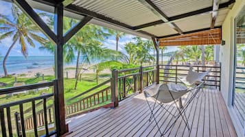 A wooden deck with a hammock, overlooking a beach with palm trees and the ocean.