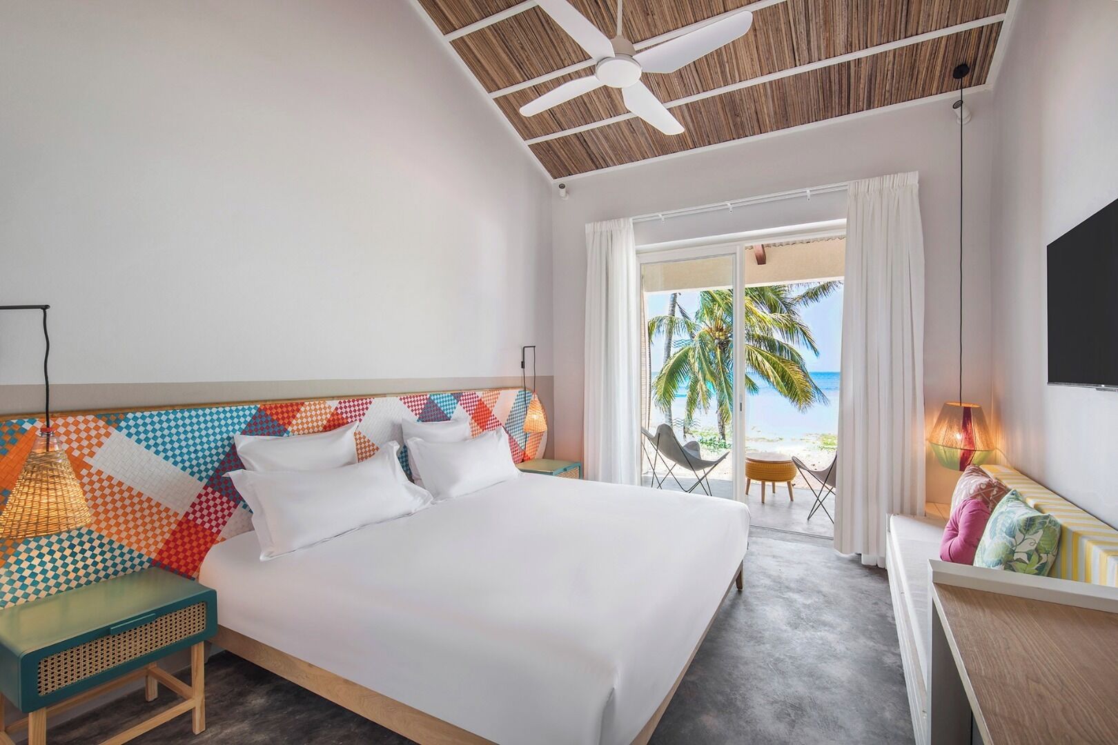 Une chambre d’hôtel avec un lit, un bureau, une chaise, un ventilateur de plafond et une vue sur la plage.